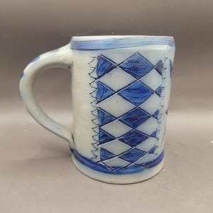 May include: A blue and white stoneware mug with a diamond pattern. The mug has a handle and is made in a traditional style.