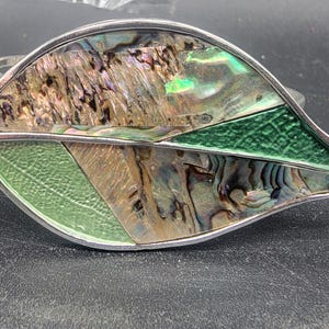 May include: A silver leaf-shaped bracelet with green and iridescent abalone shell inlay.
