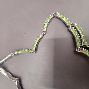 May include: A silver necklace with a double row of green stones. The necklace is made of small, round stones that are set in a silver setting.