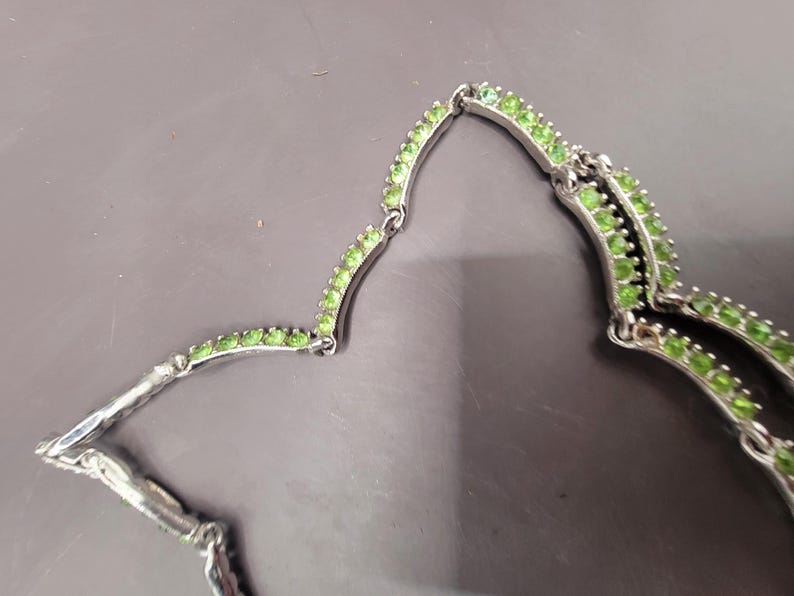 May include: A silver necklace with a double row of green stones. The necklace is made of small, round stones that are set in a silver setting.