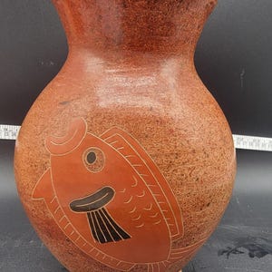 May include: A terracotta vase with a stylized fish design in black and orange. The vase has a wide mouth and a rounded body.
