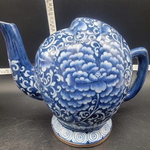 May include: A blue and white ceramic teapot with a floral design. The teapot has a round body and a spout on the side. The teapot is decorated with a blue and white floral pattern.