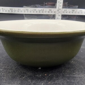 May include: A green and white ceramic bowl. The bowl has a white interior and a dark green exterior.