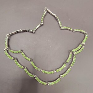May include: A silver necklace with two rows of green stones. The necklace is made of a chain with small, curved pieces that are connected by green stones.