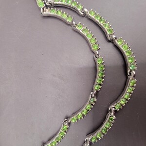 May include: A silver necklace with three rows of green gemstones. The necklace is made of a delicate chain with small, round gemstones.
