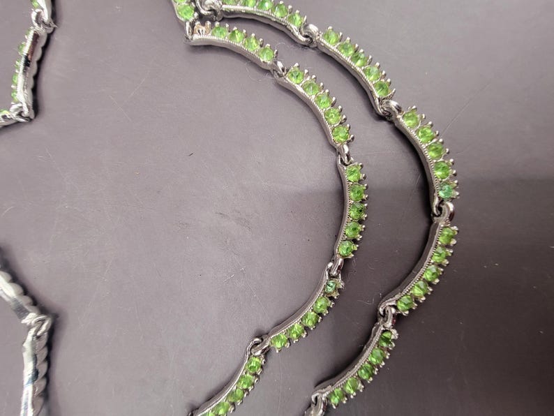 May include: A silver necklace with three rows of green gemstones. The necklace is made of a delicate chain with small, round gemstones.