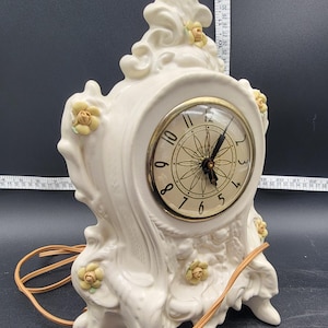 May include: White porcelain clock with a gold-toned face and black hands. The clock is decorated with yellow roses and has a cord for plugging in.