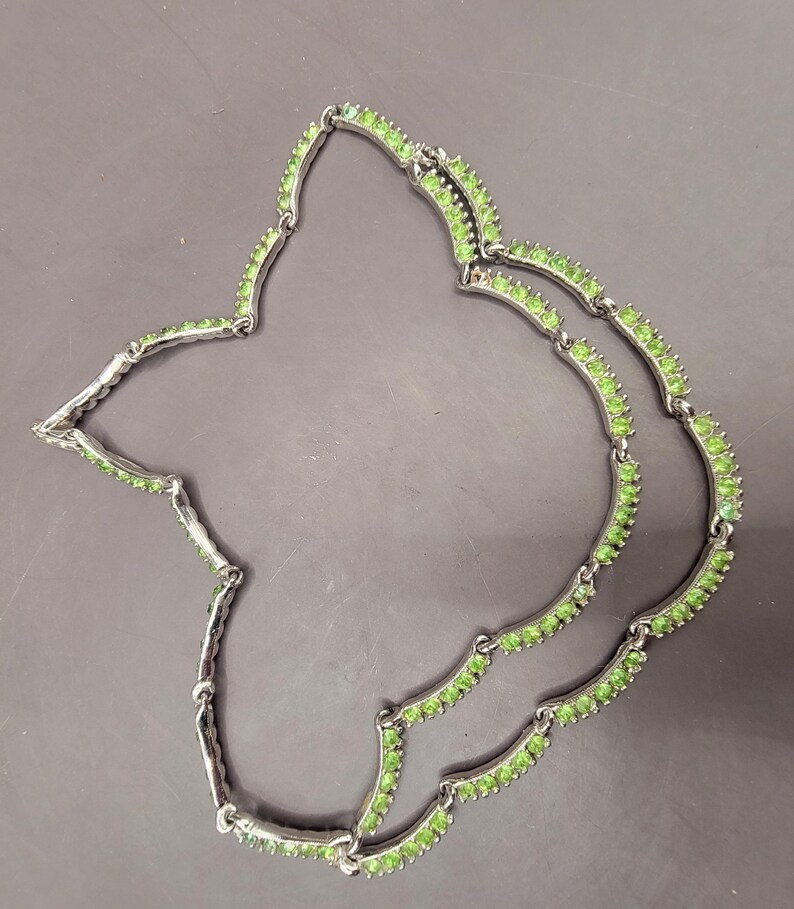 May include: A silver necklace with two rows of green stones. The necklace is made of small, round stones that are set in a silver setting. The necklace is a delicate and elegant piece of jewelry.