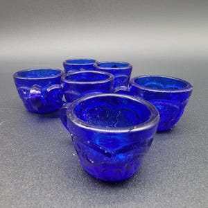 Puede incluir: Juego de seis tazas de vidrio azul cobalto con un diseño decorativo. Las tazas tienen una pequeña asa y son perfectas para servir pequeñas porciones de comida o bebida.