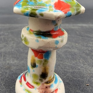 May include: A ceramic mushroom figurine with a white base and stem, and a colourful cap. The cap is painted with red, blue, and green spots. The figurine is approximately 7.6 cm tall.
