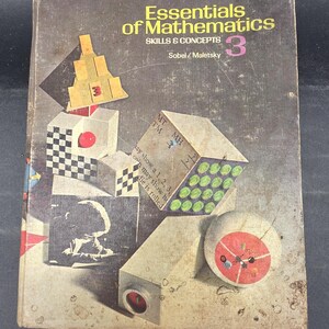 May include: A vintage textbook titled "Essentials of Mathematics" with the number 3 prominently displayed. The cover features geometric shapes in various colors, including yellow, red, and green, against a weathered gray background. The book's title and author are also visible.