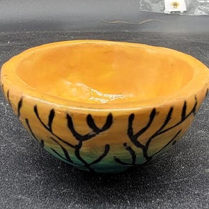 May include: A small, orange ceramic bowl with a black and blue design of tree branches. The bowl is handmade and has a rustic look.