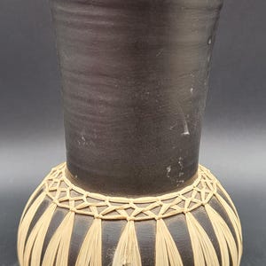 Może przedstawiać: Czarny ceramiczny wazon z plecionym wzorem wokół środka. Wazon ma szeroki otwór i zaokrąglone ciało.