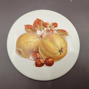Peut inclure: Une assiette en céramique blanche avec un motif peint à la main de deux pommes jaunes et une branche de noisettes avec des feuilles. Les pommes sont ombragées de jaune, d'orange et de brun. Les noisettes sont brunes avec des tiges rouges. Les feuilles sont vertes, orange et brunes.