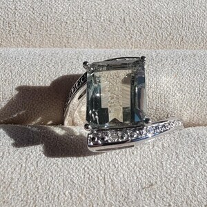 May include: A silver ring with a large, clear, emerald-cut gemstone and a band of small diamonds.