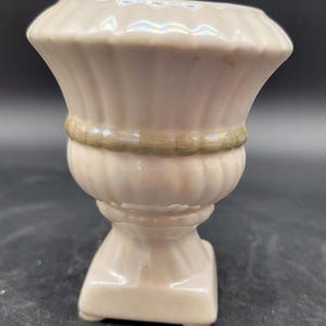 May include: A small, white ceramic planter with a fluted design and a gold band around the middle. The planter has a square base and a rounded top.