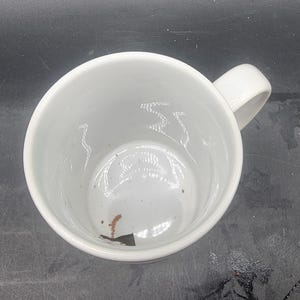 Puede incluir: Taza de cer&aacute;mica blanca con asa. La taza est&aacute; vac&iacute;a y tiene una peque&ntilde;a mancha marr&oacute;n en el interior.