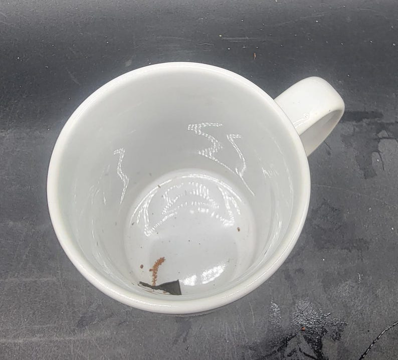 Puede incluir: Taza de cer&aacute;mica blanca con asa. La taza est&aacute; vac&iacute;a y tiene una peque&ntilde;a mancha marr&oacute;n en el interior.