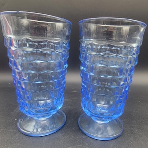 May include: Two blue glass tumblers with a textured, diamond-shaped pattern. The glasses have a flared base.