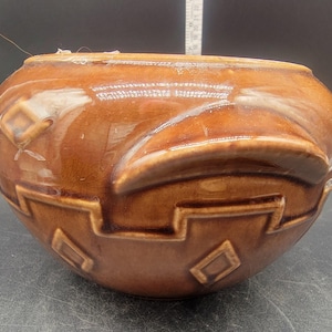 Könnte beinhalten: Ein brauner Keramiktopf mit geometrischem Muster. Der Topf hat eine abgerundete Form und eine breite Öffnung.
