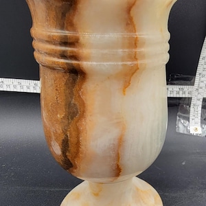 May include: A white and brown marble vase with a wide mouth and a round base. The vase has a unique marbled pattern with brown and white streaks.