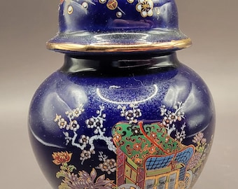 Peut inclure: Un pot en porcelaine bleu cobalt avec un couvercle, décoré de bordures dorées et d'un motif floral. Le pot représente une scène de calèche tirée par des chevaux avec des fleurs de cerisier.