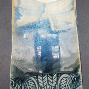 Op de afbeelding: Een keramische schaal met een blauwe en witte glazuur. De schaal heeft een decoratief patroon van bladeren en spiralen. De schaal is rechthoekig en heeft een licht gebogen rand.