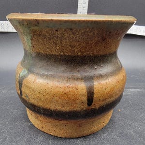 May include: A small, brown, ceramic planter with a wide, flared opening and a narrow base. The planter has a brown, black, and green glaze with a drip effect.
