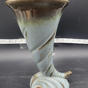 May include: A blue and brown ceramic vase shaped like a horn. The vase has a swirl design and a wide opening.