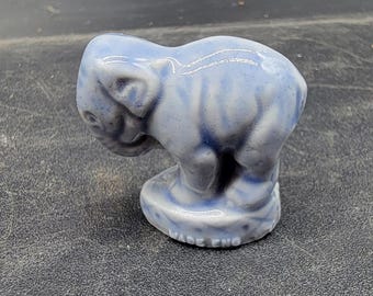 May include: A small, light blue ceramic elephant figurine with dark blue accents. The elephant is in a standing position with its trunk down. The base of the figurine reads "MADE ENG".
