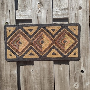 May include: A rectangular rug featuring a textured hooked yarn construction with a repeating geometric pattern of diamonds and triangles in shades of dark charcoal, mustard yellow, burnt orange, and muted brown tones throughout the design.