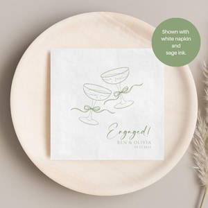 May include: A white square paper napkin featuring a sage green line art illustration of two champagne glasses tied with ribbons. The text reads Engaged! followed by the names Ben & Olivia and the date 09.27.2025 in sage green ink.