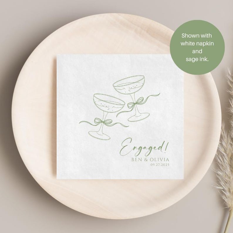 May include: A white square paper napkin featuring a sage green line art illustration of two champagne glasses tied with ribbons. The text reads Engaged! followed by the names Ben & Olivia and the date 09.27.2025 in sage green ink.