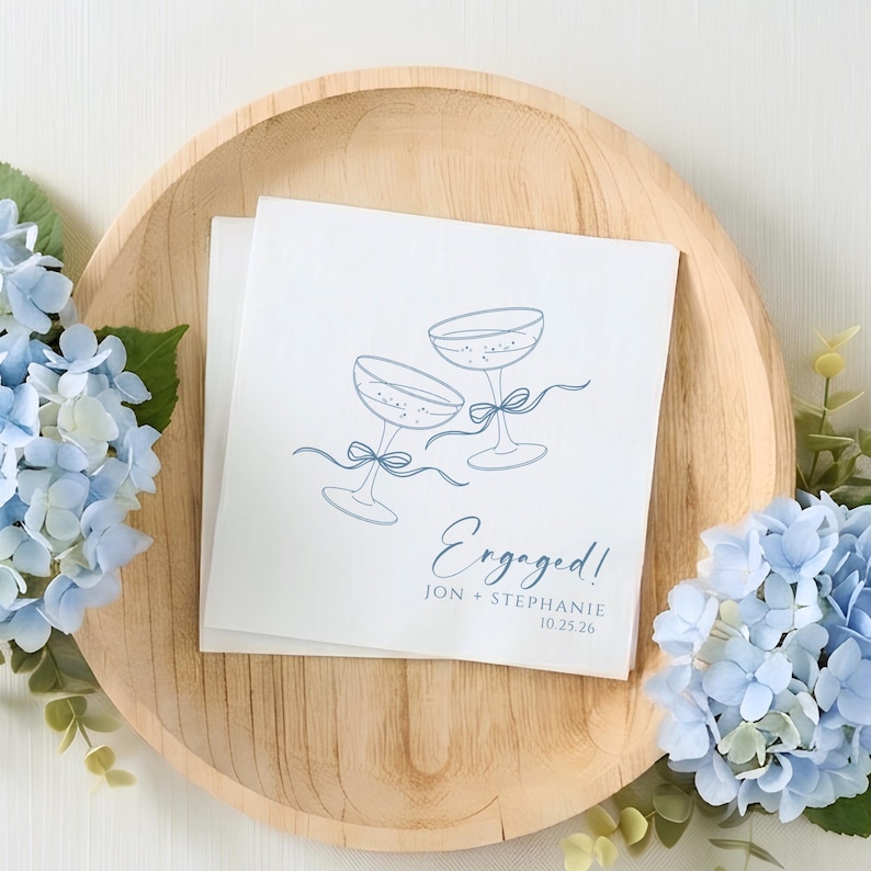 Custom napkins for engagement party featuring champagne toast graphic personalized with the couple's names and wedding or engagement date.