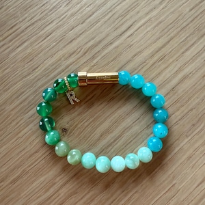 May include: A green and blue gemstone bracelet with a gold charm that says "Infinity".
