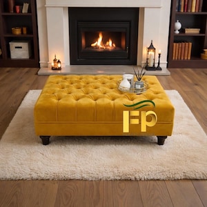May include: A mustard yellow, button-tufted ottoman with dark wooden legs on a cream rug. The square ottoman is in front of a fireplace with a burning fire. A decorative tray with vases and a diffuser sits on top.
