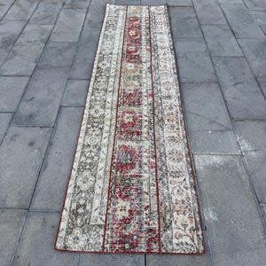 May include: A vintage runner rug with a red, white, and brown geometric pattern. The rug has a faded, distressed look and is perfect for adding a touch of bohemian style to your home.