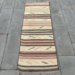 May include: A long, narrow rug with a striped pattern in shades of brown, beige, and pink. The rug has a fringe border and features a geometric design.