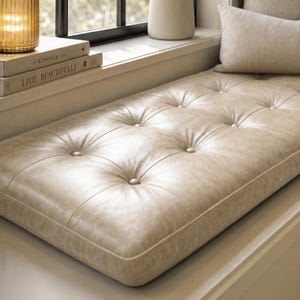 May include: A rectangular beige bench cushion featuring a tufted button design across its surface. The cushion has a smooth, textured finish and is positioned horizontally, showcasing a structured edge with piping detail along the perimeter.