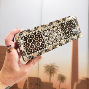 May include: A rectangular box with a decorative inlaid design made of mother of pearl and black wood. The box has a geometric pattern with a variety of shapes and sizes.