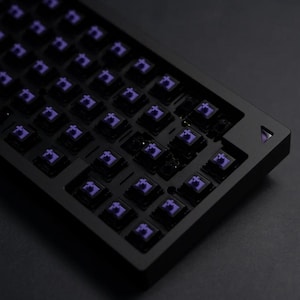 May include: A black mechanical keyboard with a full layout of purple keycaps. The keyboard has a minimalist design with a black frame and a black keycap base.