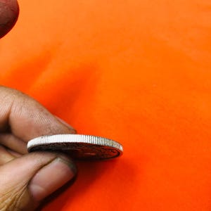 May include: A silver coin with a raised rim and a design on the front side.