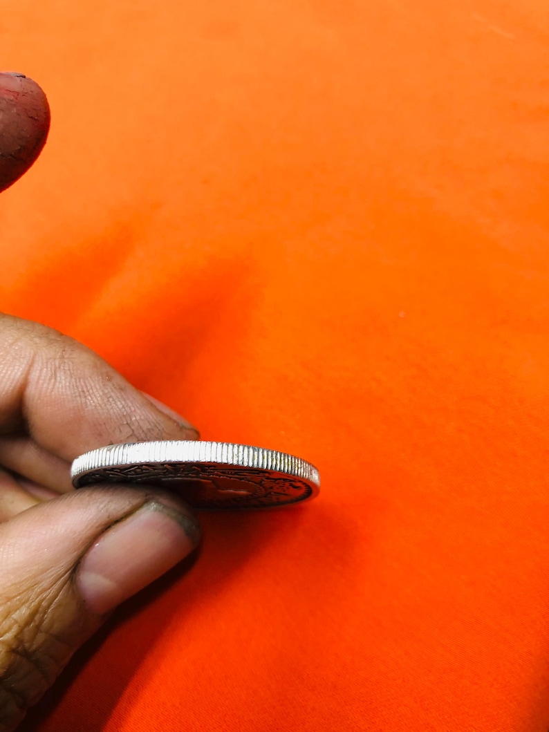 May include: A silver coin with a raised rim and a design on the front side.