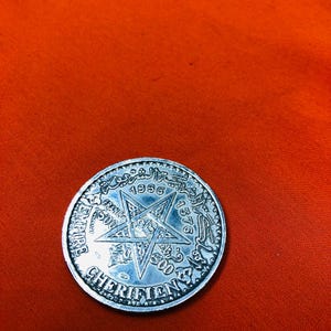 May include: A silver coin with a five-pointed star in the center and the text "1376 1956" around the star. The text "EMPIRE CHERIFIEN" is around the edge of the coin.