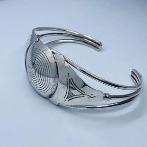 Peut inclure: Bracelet en argent avec un motif en spirale et un motif géométrique. Le bracelet est composé de trois bandes d'argent.