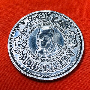 May include: Silver coin with a portrait of a man wearing a hat and the text "MOHAMMED V" around the edge.