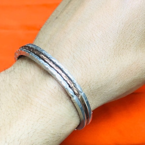 Peut inclure: Un bracelet en argent et cuivre avec une texture martelée. Le bracelet est composé de trois bandes, la bande en cuivre étant au milieu.