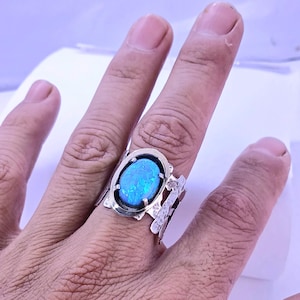 Peut inclure: Une bague en argent ornée d'une pierre précieuse ovale bleue irisée. La bague a un anneau texturé avec un motif décoratif sur les côtés. La pierre est sertie dans une lunette en argent.