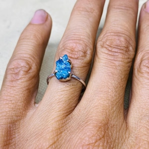 Peut inclure: Bague en argent ornée d'une pierre brute bleu clair. La pierre précieuse est de forme irrégulière et sertie dans un design simple et minimaliste. La bague est portée au doigt.