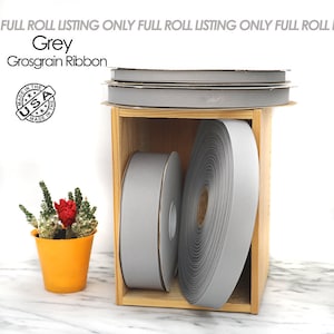 Könnte beinhalten: Drei Rollen graues Grosgrainband in einer Holzkiste. Das Band ist in den USA hergestellt.
